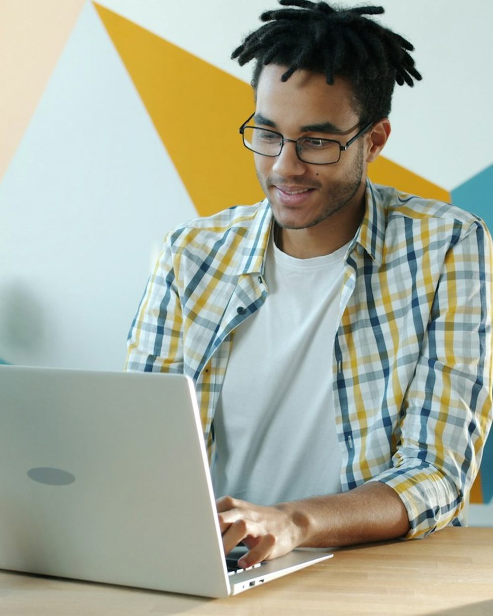 A young man smiling as he works on a laptop at home